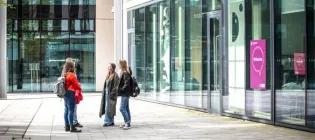 Four students chatting outside a glass building