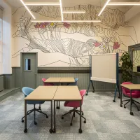 A room with tables and chairs, a pinboard on wheels, one wall has a large pattern of pink and white flowers