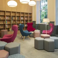 A room with four high back chairs, grey and pink stools and a bookcase built into the wall