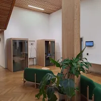 A room with a large pillar and green sofa, a green plant and two meeting pod
