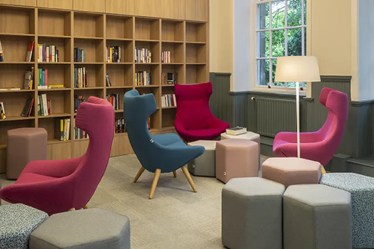 A room with four high back chairs, grey and pink stools and a bookcase built into the wall