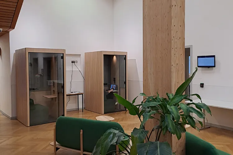 A room with a large pillar and green sofa, a green plant and two meeting pod